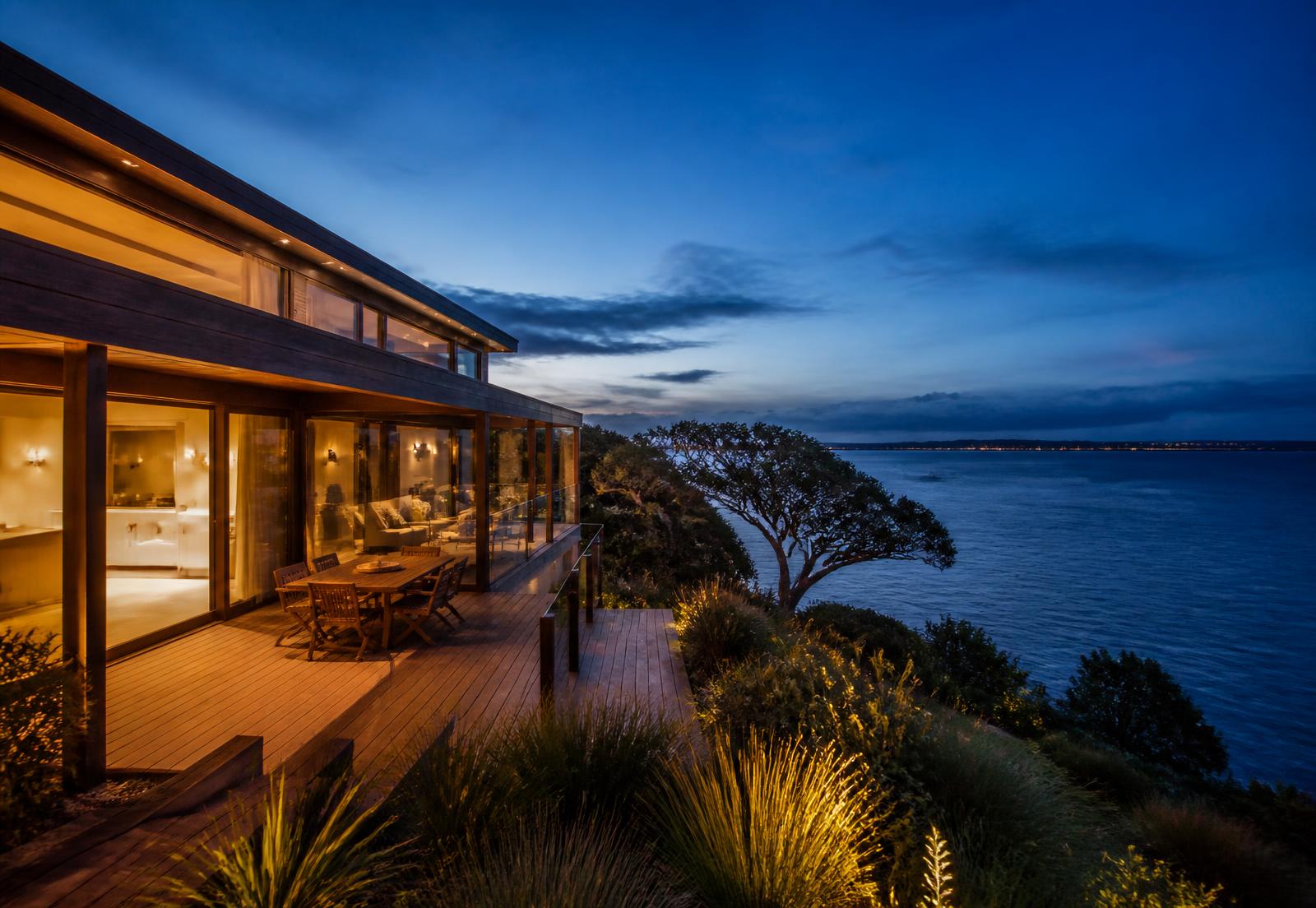 Modern Auckland coastal home with a timber deck overlooking the Hauraki Gulf at dusk